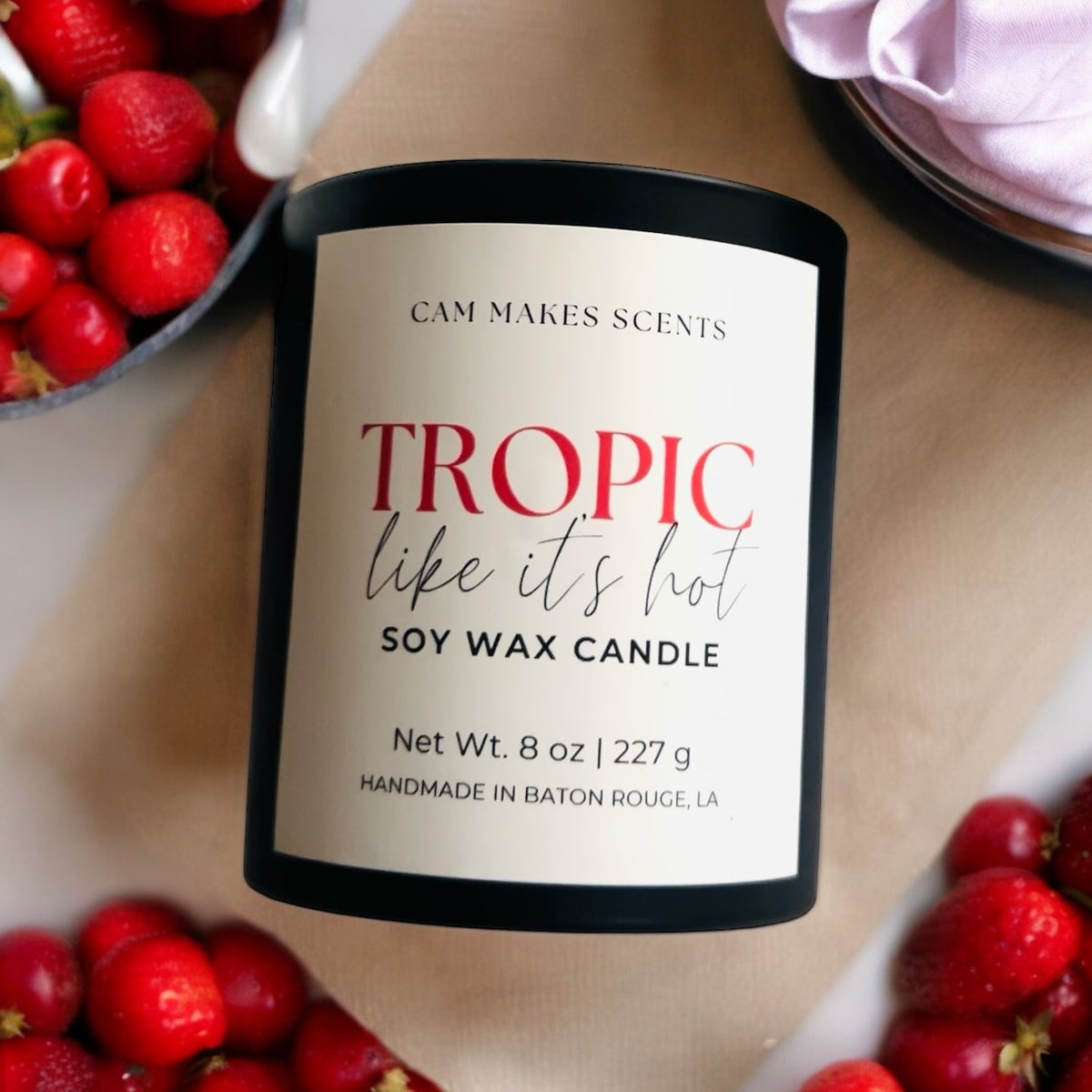 8 oz soy wax candle in a black jar lying on table surrounded by bowls of red fruit. 